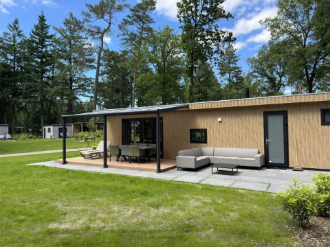 Moderne Veluwe Villa lodge met houten afwerking, tuinset en eettafel, omgeven door bos en gras.