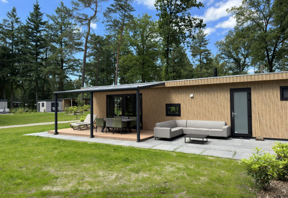 Moderne Veluwe Villa lodge met houten afwerking, tuinset en eettafel, omgeven door bos en gras.