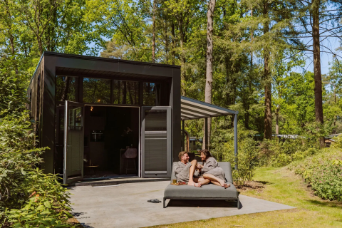 Paar entspannt sich vor der Veluwe Suite mit Sauna auf Camping Samoza, umgeben von Wald in den Niederlanden.