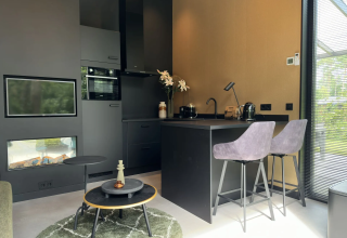 Moderne compacte lodgekeuken met zwart interieur, ontbijtbar en haard in Veluwe Suite met sauna, Samoza.