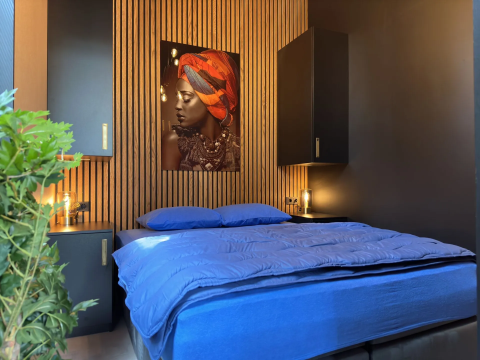 Moderne slaapkamer in Veluwe Suite met sauna bij Camping Samoza, blauw beddengoed en houten wand.