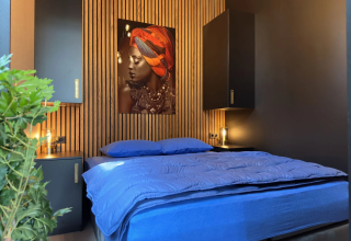 Moderne slaapkamer in Veluwe Suite met sauna bij Camping Samoza, blauw beddengoed en houten wand.