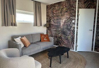 Soggiorno moderno alla Zonneweelde Lodge Deluxe al Camping Zonneweelde, con divano grigio e parete artistica.