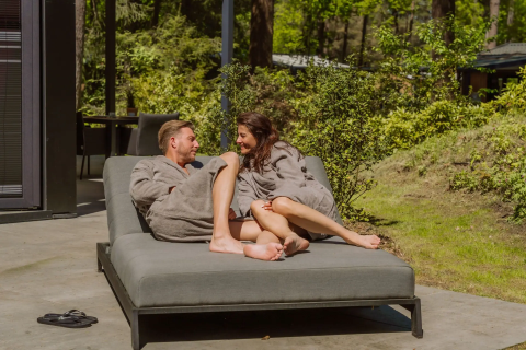 Paar in Bademänteln entspannt auf einer Liege vor Veluwe Suite mit Sauna bei Camping Samoza in den Niederlanden.