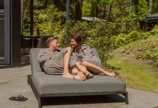 Paar in Bademänteln entspannt auf einer Liege vor Veluwe Suite mit Sauna bei Camping Samoza in den Niederlanden.