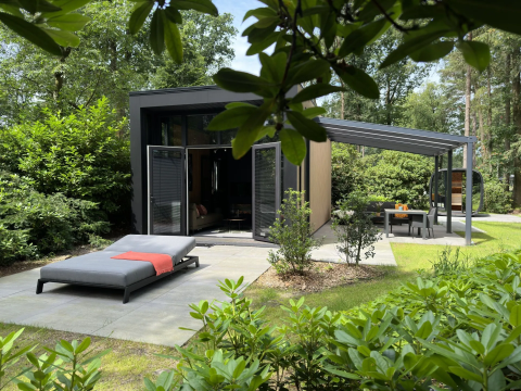 Moderne Lodge mit Sonnenliege und Essbereich draußen, umgeben von Natur im Camping Samoza, Niederlande.