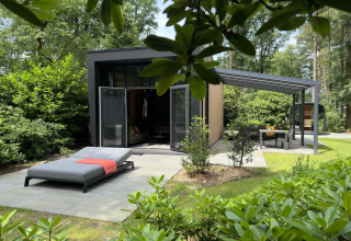 Moderne Lodge mit Sonnenliege und Essbereich draußen, umgeben von Natur im Camping Samoza, Niederlande.