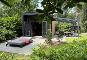 Lodge moderno con lettino prendisole e zona pranzo esterna immersi nel verde al Camping Samoza, Paesi Bassi.