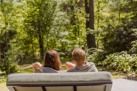 Twee mensen ontspannen op een bankje bij Veluwe Suite met sauna op Camping Samoza, genietend van de natuur.
