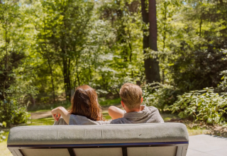 Twee mensen ontspannen op een bankje bij Veluwe Suite met sauna op Camping Samoza, genietend van de natuur.