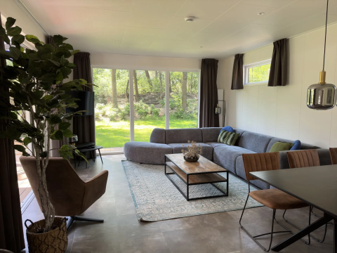 Moderne woonkamer in Veluwe Villa op Camping Samoza, Nederland, met grote ramen en zicht op bos.