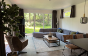 Moderne stue i Veluwe Villa på Camping Samoza i Holland med store vinduer, grøn sofa og naturudsigt.