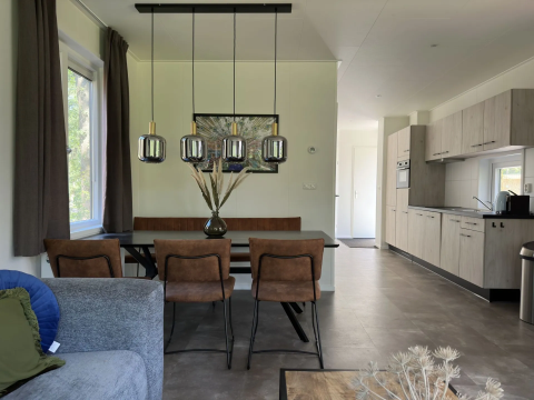 Modern lodge-interieur met eettafel, bruine stoelen, hanglampen en open keuken in Veluwe Villa.