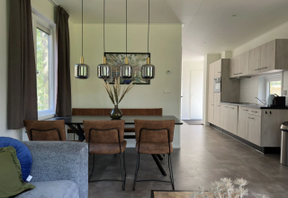 Modern lodge-interieur met eetafel, bruine stoelen, hanglampen en open keuken in Veluwe Villa.