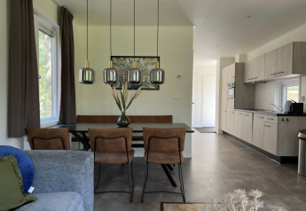 Interno di lodge moderno con tavolo da pranzo, sedie marroni, lampade a sospensione e cucina aperta.