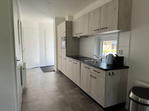 Moderne keuken met lichte houten kasten, oven, raam en apparatuur in Veluwe Villa op Camping Samoza.