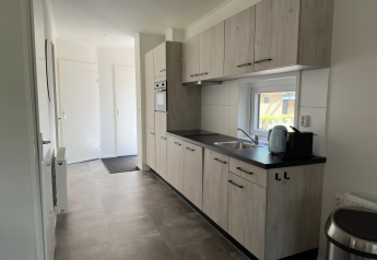 Cucina moderna con mobili in legno chiaro, forno, finestra e elettrodomestici nella Veluwe Villa di Camping Samoza.