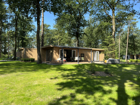 Veluwe Villa-lodge op Camping Samoza in Nederland, omringd door hoge bomen en een groen gazon.