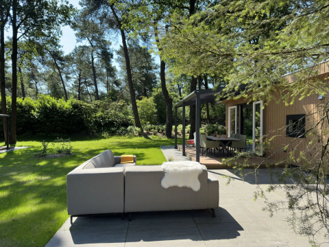 Buitenhoek met loungebank bij Veluwe Villa op Camping Samoza in Nederland, omgeven door bosrijk groen.