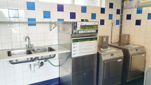 Gemeenschappelijke wasruimte bij glamping met twee wasmachines, afwasmachine en dubbele spoelbak.