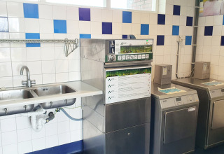 Gemeenschappelijke wasruimte bij glamping met twee wasmachines, afwasmachine en dubbele spoelbak.