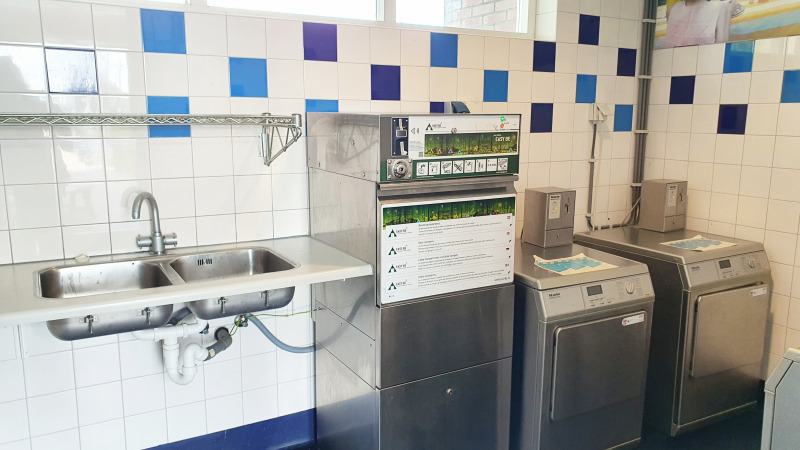 Communal laundry room at a glamping site with two washing machines, a dishwasher, and a double sink.