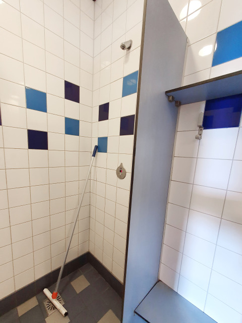 Shower area with blue and white tiles and a mop in the Water bubbles tiny house at Marina Parcs Almere.