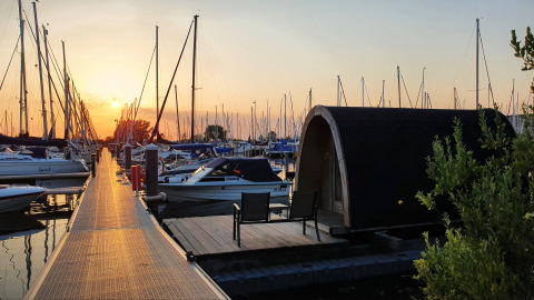 Solnedgang over både og tiny house ved vandkanten på Water Bubbles, Marina Parcs Almere, Holland.