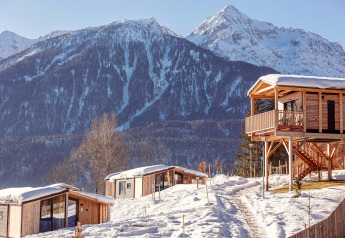 Gemütliche Holzhütten im verschneiten Gebirge, sonnige Winterlandschaft mit imposanten Alpen im Hintergrund.
