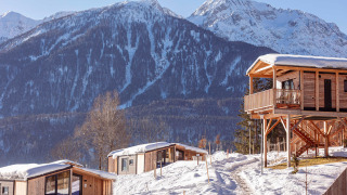 Knusse houten chalets in een besneeuwd berglandschap, met majestueuze pieken en een heldere winterlucht.