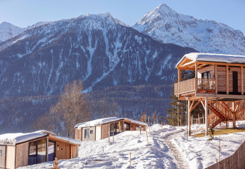 Chalet in legno immersi nella neve, con maestose montagne sullo sfondo e cielo invernale limpido e sereno.