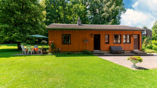 Foto van een gezellige houten lodge bij Les Bouleaux met grasveld, bomen en tuinmeubilair buiten.