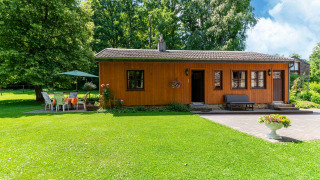 Photo of a cozy wooden lodge at Les Bouleaux, surrounded by green lawn, trees, and garden furniture.