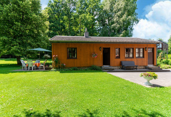 Foto van een gezellige houten lodge bij Les Bouleaux met grasveld, bomen en tuinmeubilair buiten.