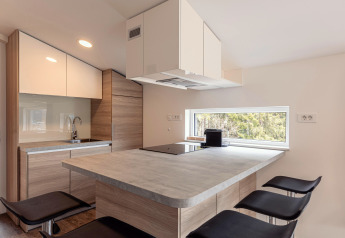 Moderne compacte keuken met houtelementen en groot raam in Chalets & Glamping Nassfeld 1, Oostenrijk.