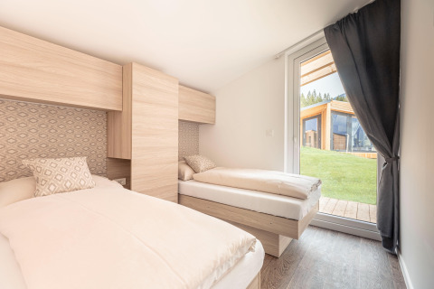 Camera luminosa con due letti singoli e grande finestra presso Chalets & Glamping Nassfeld 1, Austria.