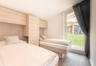 Camera luminosa con due letti singoli e grande finestra presso Chalets & Glamping Nassfeld 1, Austria.