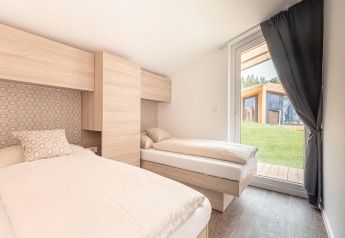 Lichte slaapkamer met twee eenpersoonsbedden en groot raam in Chalets & Glamping Nassfeld 1, Oostenrijk.