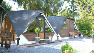 Vue extérieure du chalet Mise Au Vert avec toits triangulaires, verdure, arbres et cour en gravier.