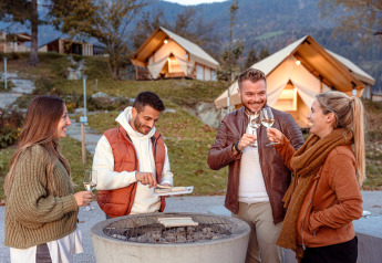 Vier vrienden drinken wijn en barbecueën buiten bij luxe tenten van Chalets & Glamping Nassfeld 1 in Oostenrijk.