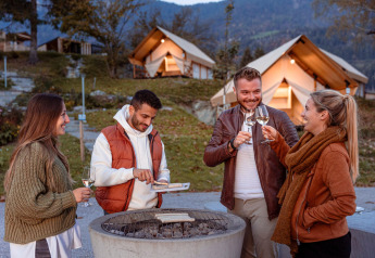 Vier vrienden drinken wijn en barbecueën buiten bij luxe tenten van Chalets & Glamping Nassfeld 1 in Oostenrijk.