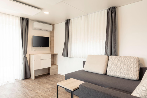 Moderne stue med sofa, TV, bord og store vinduer i et chalet på Chalets & Glamping Nassfeld 2 i Østrig.