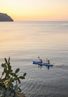 Twee mensen kajakken bij zonsondergang op rustig water, omgeven door bomen in een glampingpark.