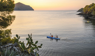 Due persone in kayak al tramonto su acque tranquille circondate da alberi in un parco glamping.