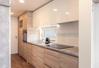 Modernes, helles Chalet-Küche mit Holzfronten, Fenster, Induktionskochfeld, Mikrowelle und Backofen in Österreich.