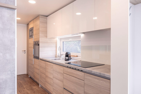 Moderne, lyst køkken med træskabe, ovn, mikroovn og stort vindue, i Chalet «& Glamping Nassfeld 2», Østrig.