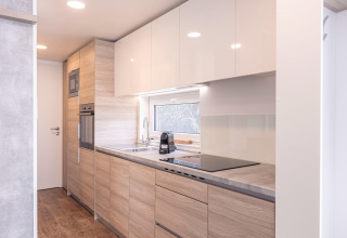 Moderne, lyst køkken med træskabe, ovn, mikroovn og stort vindue, i Chalet «& Glamping Nassfeld 2», Østrig.