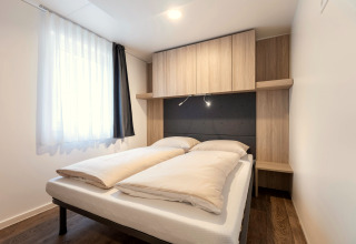 Modernes Schlafzimmer mit Doppelbett, Holzmöbeln und Tageslicht in Chalets & Glamping Nassfeld 2, Österreich.