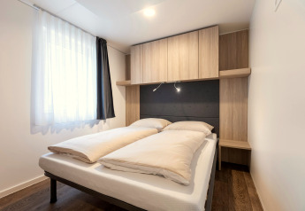 Moderne slaapkamer met tweepersoonsbed, houten kasten en daglicht in Chalets & Glamping Nassfeld 2, Oostenrijk.