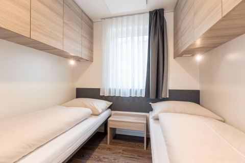 Moderne soveværelse med to enkeltsenge, lyse træskabe og stort vindue i Chalets & Glamping Nassfeld 2, Østrig.
